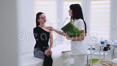 年轻的黑发女人穿着优雅的衣服坐在美容师€™的<strong>柜子</strong>里，美容师检查她的脸，他们