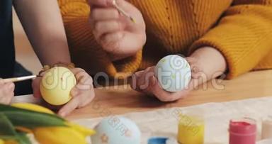 妈妈和女儿用手把复活节彩<strong>蛋</strong>用颜色和刷子贴紧。 五颜六色的复活节彩<strong>蛋</strong>。 筹备工作