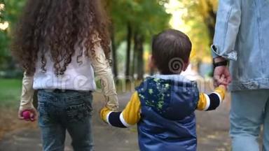 幸福的家庭，妈妈和孩子们牵手散步。 家庭的概念，母亲和年轻人一起在公园散步