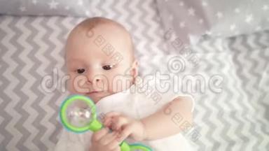 可爱的小男孩玩玩具的肖像。 可爱的孩子在床上玩拨浪鼓