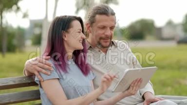 放松迷人的中年男子，留着长长的灰色头发，一个年轻的女人，染着头发，拥抱着，看着一张照片。