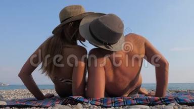 快乐的年轻夫妇在海滩上晒太阳，躺在她的背上亲吻