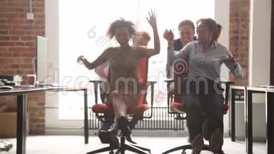 快乐的多元文化办公室工作人员笑着玩着骑在椅子上