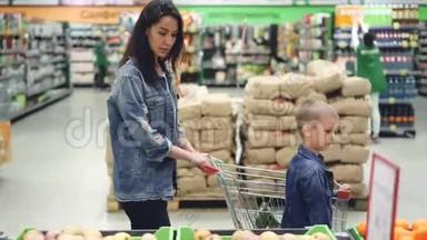 家庭欢乐的侧面景色妈妈和儿子在超市里散步，用购物手推车选择水果和交谈