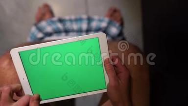 人<strong>坐</strong>在休息室的锅上.. 手握平板电脑，放大并滑动。 绿色屏幕。 单独在WC或<strong>厕</strong>所。 裤子