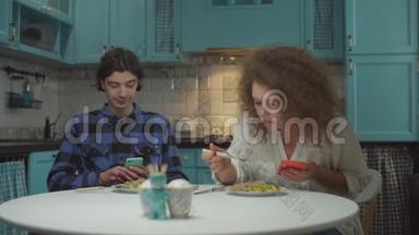 20多岁的年轻人在蓝色厨房里用小玩意吃饭时互相嘴。 男人和女人一起吃饭