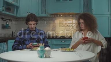 20多岁的年轻人在蓝色厨房里用小玩意<strong>吃饭</strong>时互相嘴。 男人和女人一起<strong>吃饭</strong>