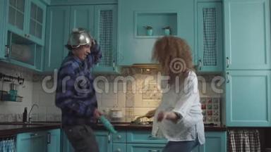 年轻快乐的20多岁夫妇穿着休闲服装，在舒适的蓝色厨房里手里拿着厨具玩。 男人和卷发女人