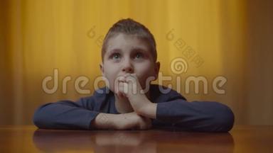 自闭症男孩坐在办公桌前表现情绪的肖像。 有自闭症的孩子在家里笑得开心