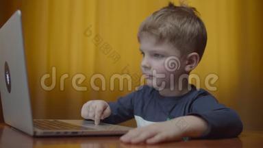 金发的学龄前男孩在笔记本电脑上打字，微笑着看着电脑屏幕。 孩子在家坐在<strong>网上学习</strong>