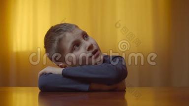 自闭症男孩坐在办公桌前表现情绪的肖像。 患有自闭症的孩子闭着眼睛是因为