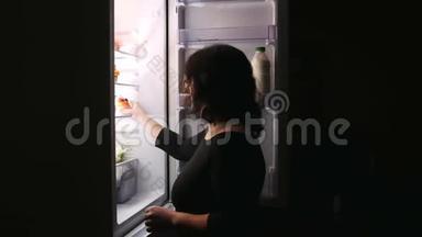 一个女人打开冰箱门拿蛋糕。 在黑色的背景上。