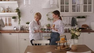 年轻女子和年迈的母亲在<strong>家中</strong>的现代厨房喝茶。