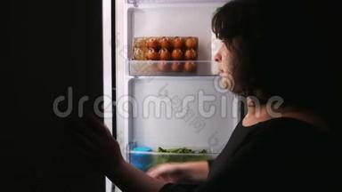 一个女人从冰箱里得到一个纸杯蛋糕。 打开并关闭冰箱门。