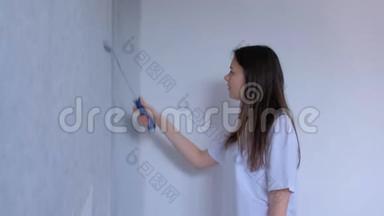 单身的年轻女孩画家是用平滚筒在灰色的墙壁上作画。