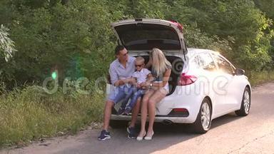 有儿子的父母坐在空路上的汽<strong>车后备箱</strong>里。 家人在度假。