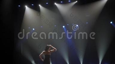 一位美丽的歌手在蓝色聚光灯下的黑暗中在舞台上摆姿势。