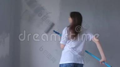 年轻的女画家正在用油漆滚筒和<strong>舞蹈</strong>用灰色油漆<strong>墙</strong>壁。