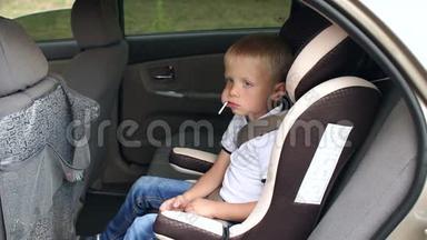 一个可爱的小男孩坐在车里的汽车座椅上，吃一根棒棒糖。