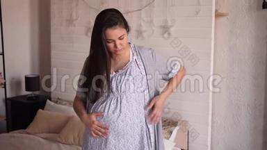 在卧室里有胃痛或背痛的悲伤孕妇穿着睡衣。