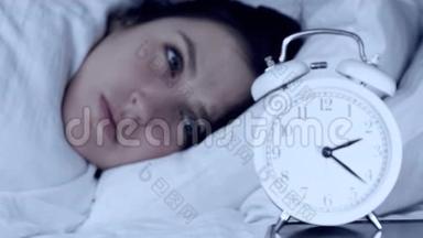 失眠，焦虑，问题的概念.. 漂亮的白种人女孩晚上躺在床上看闹钟，不能摔倒