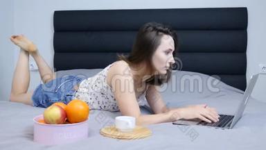 女千禧看着笔记本电脑屏幕躺在客厅的床上。 穿短裤的年轻女子在笔记本电脑<strong>上上</strong>网聊天