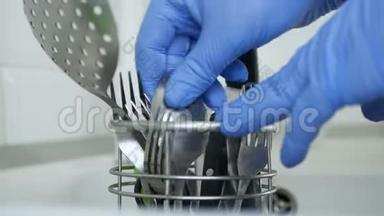 双手用橡胶手套清洗餐具，并将其置于金属支架中