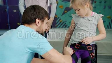 友好的攀岩教练帮助孩子在健身房室内使用安全带
