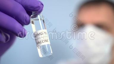 戴面膜的医生用蓝色背景的防护手套检查手中有冠状病毒疫苗的安瓿