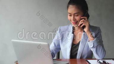年轻的亚洲妇女<strong>拿起</strong>电话，与客户谈谈工作的进展。