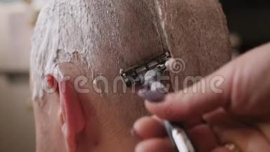 女人的手用剃须泡沫和剃须刀`男人的头刮胡子。