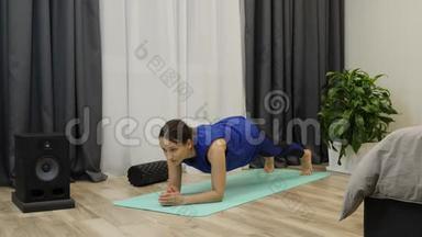 女孩在瑜伽垫上做木板姿势。 年轻健康的女运动员做木板作为她日常锻炼的一部分。 穿着潘通蓝布的女人