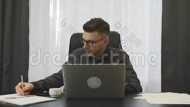 经纪人在办公室工作。 年轻的成功商人在办公室里用笔记本电脑工作。 男人在笔记本上记笔记，坐在他的屁股上