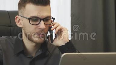 在办公室打电话的人，关闭视野。 戴眼镜的成功商人在电话里交谈，看着笔记本电脑屏幕。 港口