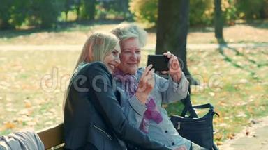 秋天，在一个美丽的公园里，年轻年老的女人在智能手机上自拍的变焦镜头