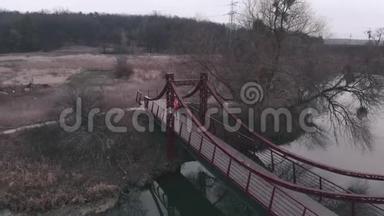 空中无人机观看女子运动员慢跑过桥。 穿橙色夹克的女人在公园里和河和桥一起跑。 <strong>体育项目</strong>