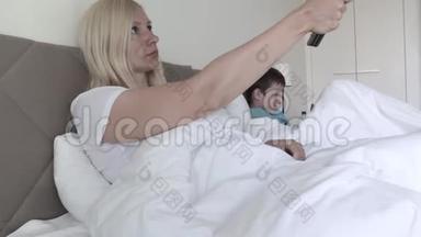 一个金发女人躺在床上，通过<strong>遥控</strong>器切换频道，她的儿子在后台玩<strong>智能</strong>手机游戏