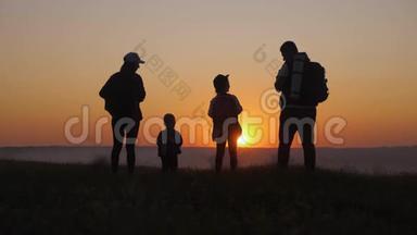 日落时父母和两个孩子在山上散步。 剪影幸福美丽的家庭