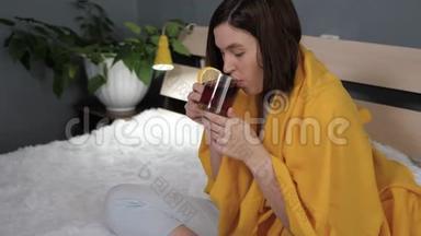 女孩在喝红茶。 迷人的年轻女人生病了，坐在床上喝柠檬茶。 感冒，流感