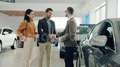 快乐的一对夫妇在经销商店里买车，和经纪人握手，抱着钥匙
