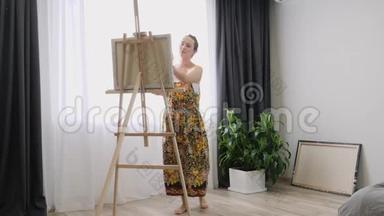 女孩艺术家在艺术工作室，站在画架后面，在画布上画画。 画画油画的年轻女子