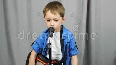 一个快乐的孩子花时间弹吉他。 一个小男孩用麦克风唱歌。 音乐、发展、生活方式