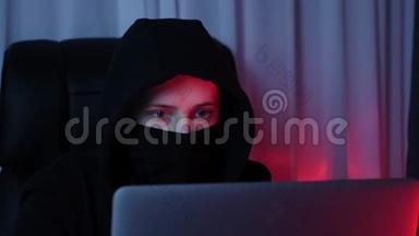女人脸上戴着黑色面具和帽衫，看着电脑屏幕，打破密码。 年轻黑客破坏了我的安全保护