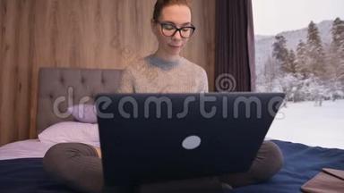 一幅有魅力的自由职业者的画像，她戴着眼镜，穿着一件毛衣，穿着长袜，坐在生态屋的床上