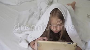 十几岁的女孩在床上玩社交网络上的平板电脑。 特写小女孩在数字平板上看视频..