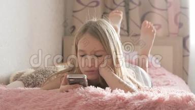 好奇的女孩使用手机应用程序看手机设备坐在床上，儿童和小工具的概念。
