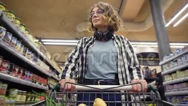 穿着格子衬衫和戴着耳机的开朗女人走在杂货店里，用食物操纵购物车