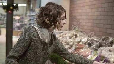 漂亮的年轻漂亮的卷发女人在超市买食物。 女孩选择蔬菜洋葱和新鲜胡萝卜