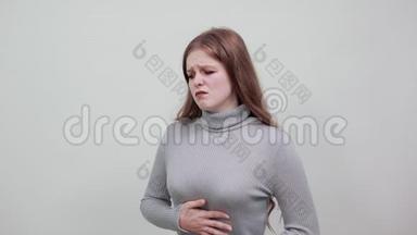 穿着灰色毛衣的年轻红发女子因肚子疼痛而身体倾斜