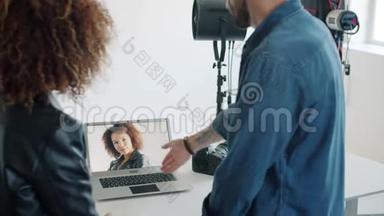 模特看着新照片和摄影棚里的摄影师交谈，看着笔记本电脑屏幕